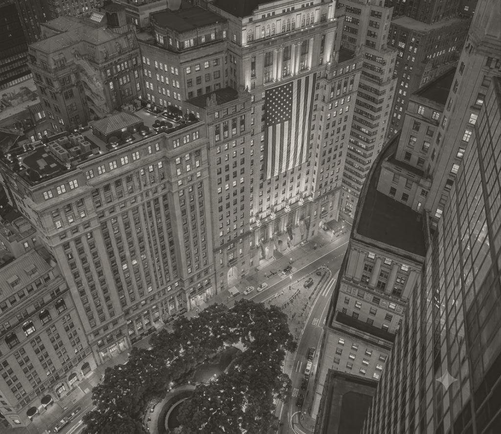 The facade of 25 Broadway at dusk with a full-height American flag hung above the entrance